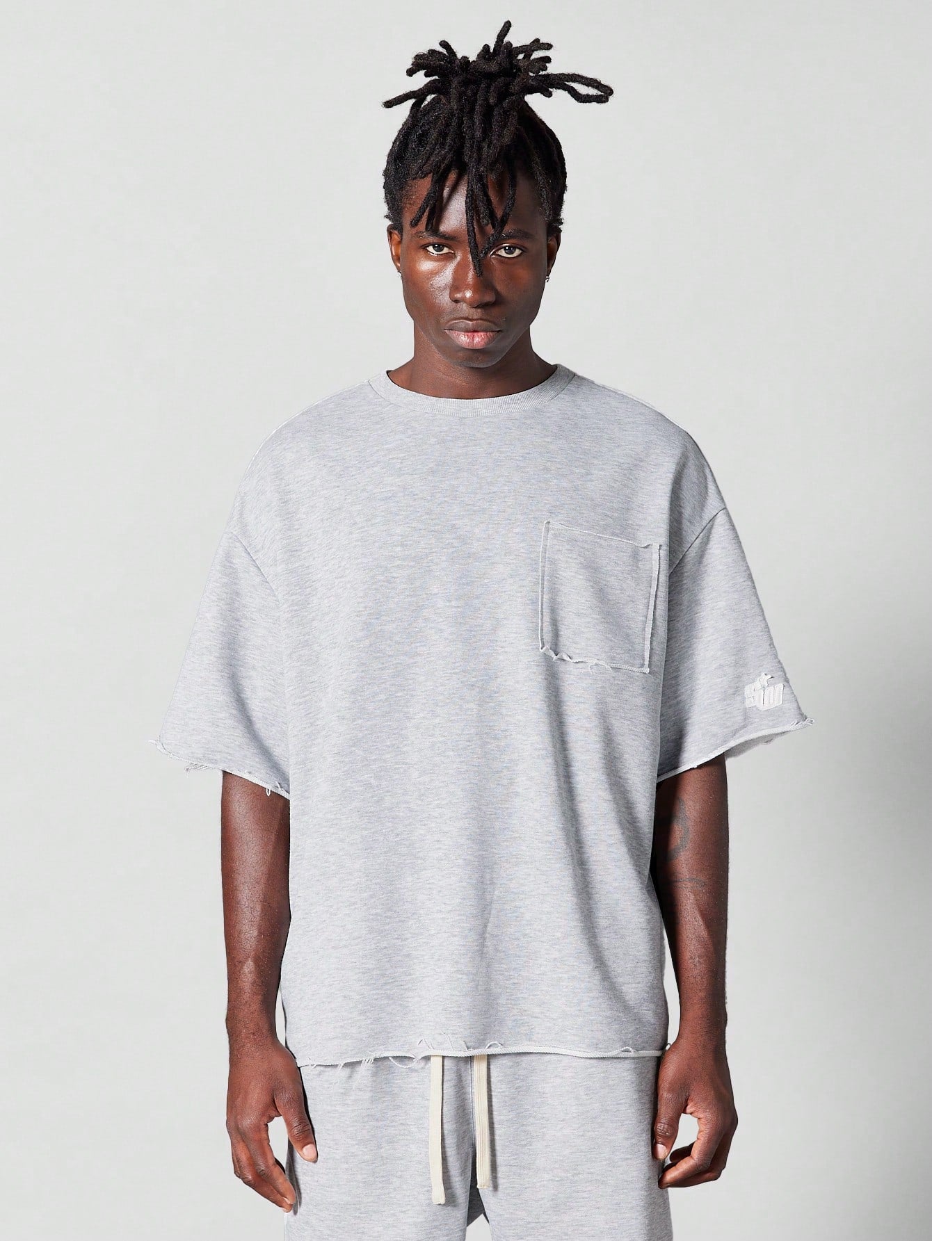 Oversized Fit Raw Edge Tee With Front Pocket And Sleeve Applique