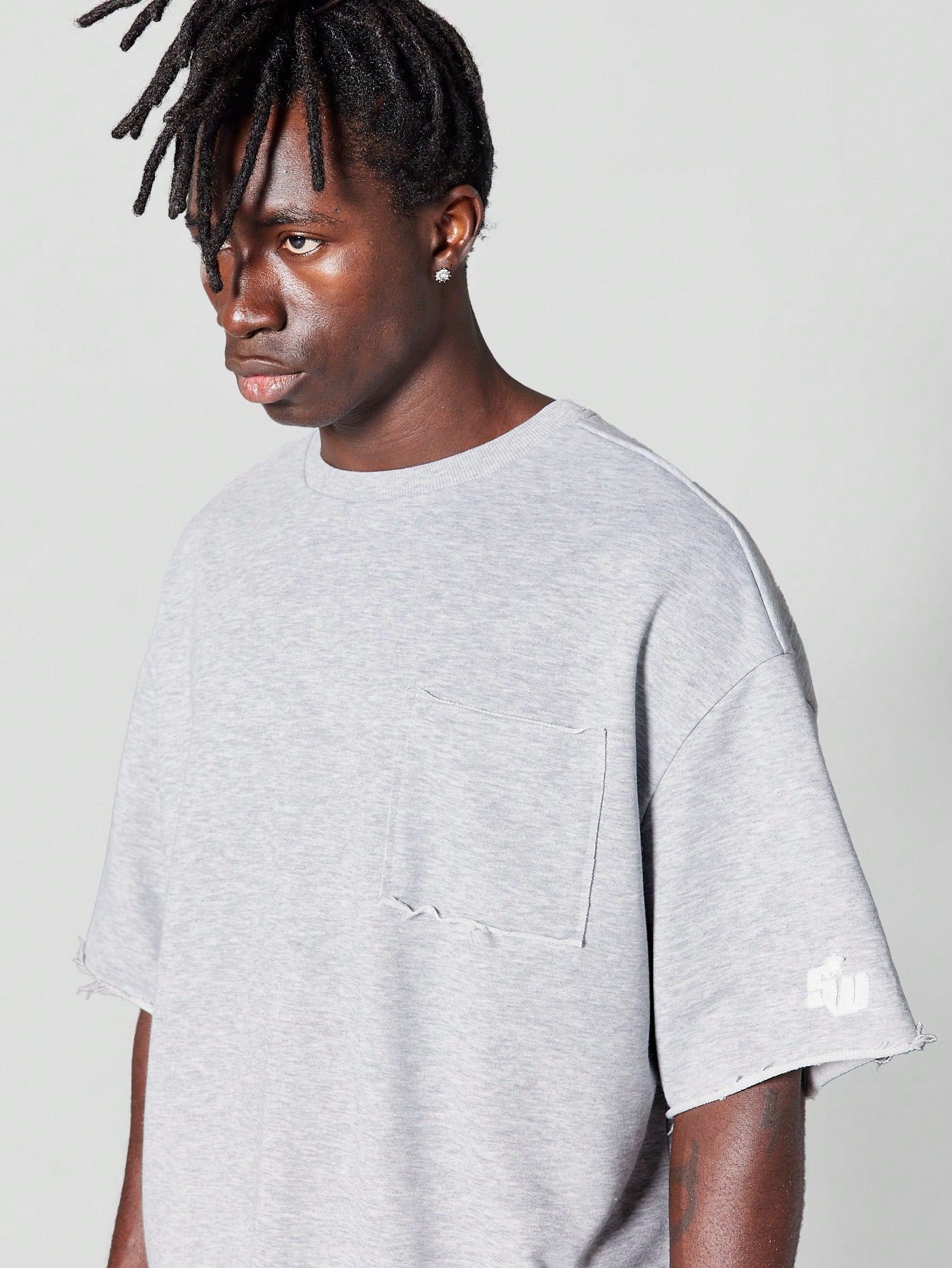Oversized Fit Raw Edge Tee With Front Pocket And Sleeve Applique